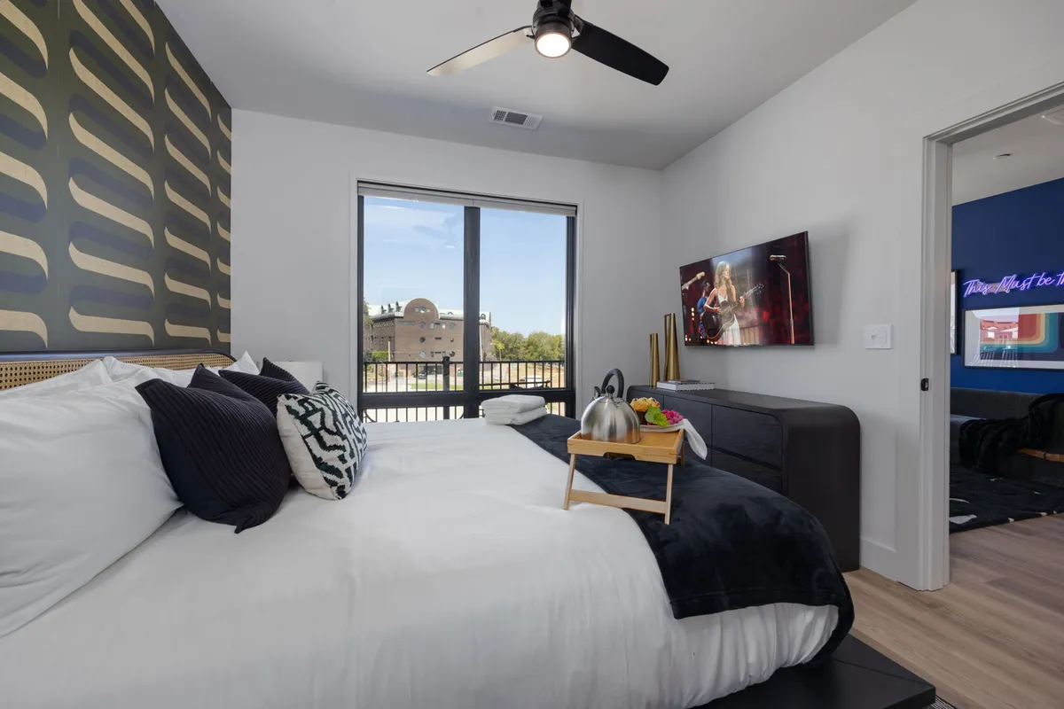 A cozy bedroom with plush pillows, a decorative feature wall, and a television in view. The mood is warm and welcoming, perfect for unwinding at the end of the day.