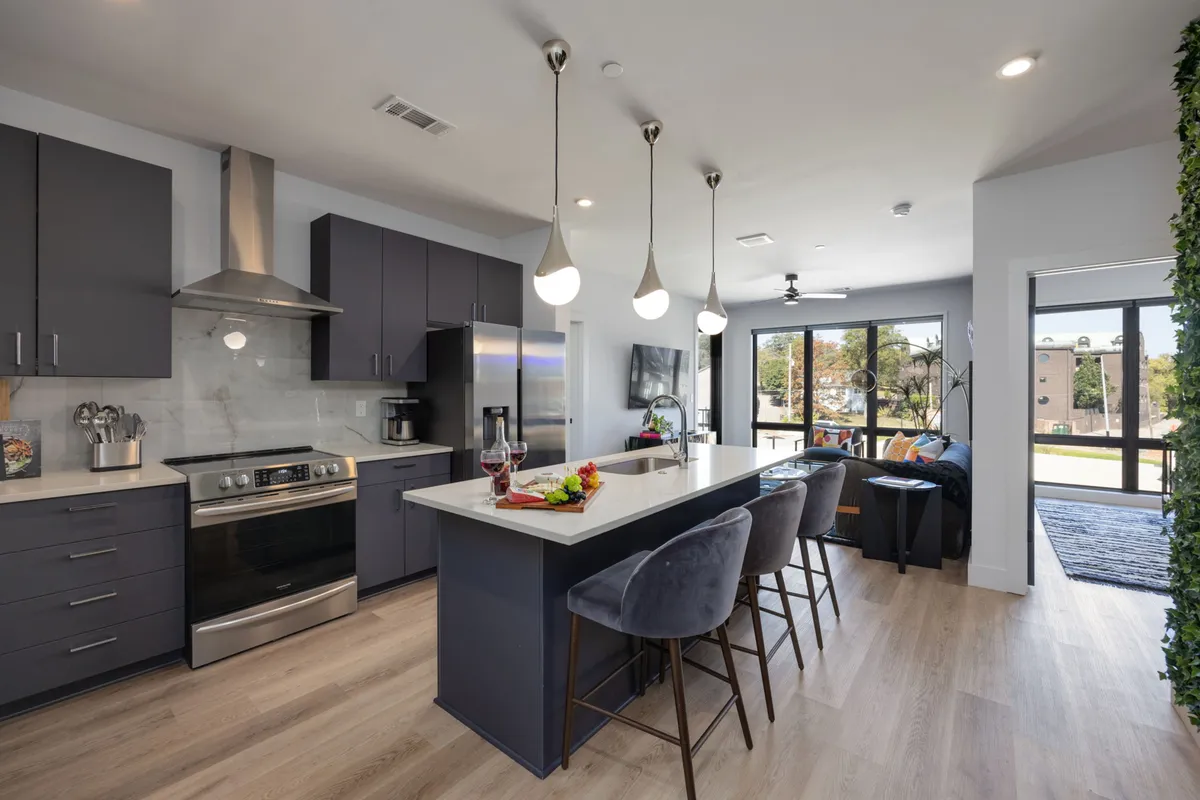 An open-plan kitchen and dining area centered around an island with bar stools, contemporary appliances, and large windows that flood the space with natural light. The inviting setting is ideal for both casual breakfasts and lively evening gatherings.