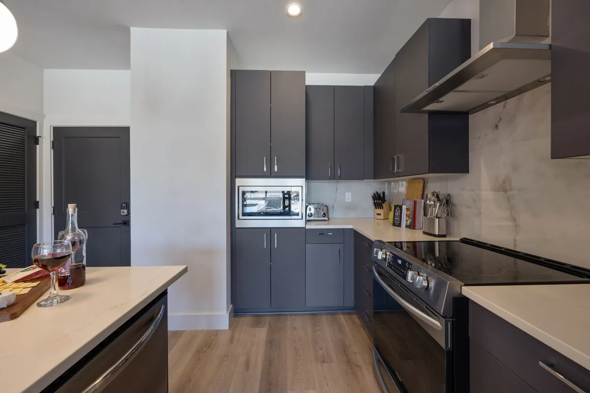 A modern kitchen scene featuring a sleek countertop adorned with glassware and snacks, complemented by stainless steel appliances and dark cabinetry. The space exudes a contemporary, inviting atmosphere that encourages both cooking and entertaining.