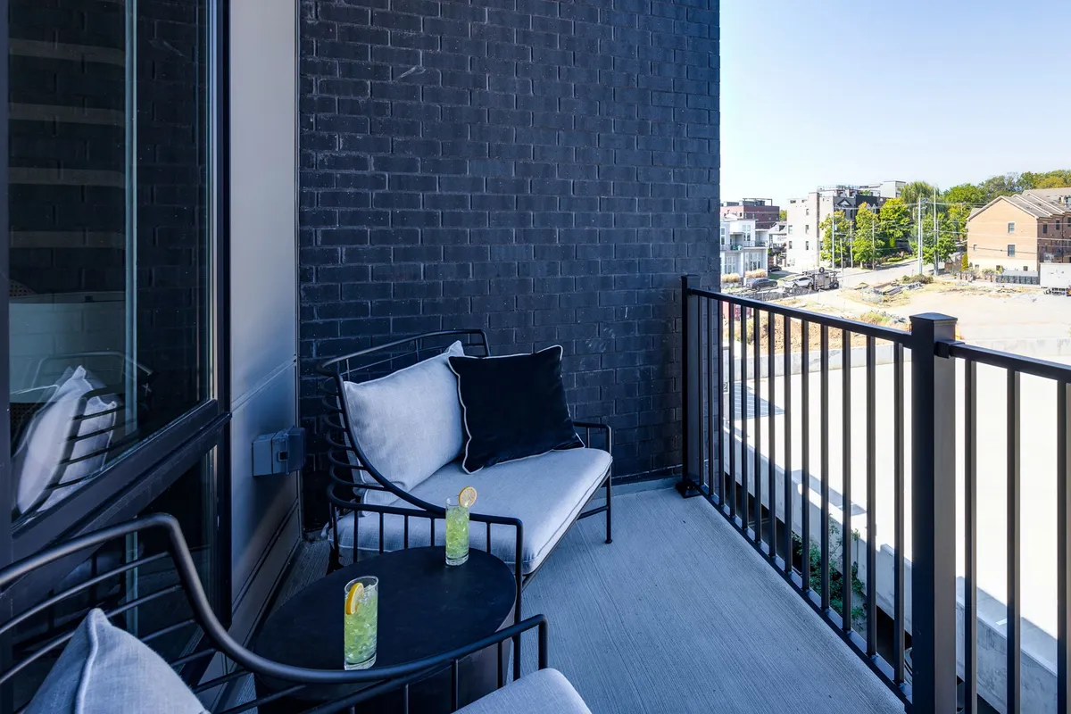 A chic private balcony setup with seating, drinks on the table, and an urban view extending beyond. The scene is serene yet sophisticated, capturing the opportunity for both quiet morning coffee and lively evening socials with the city skyline as a backdrop.