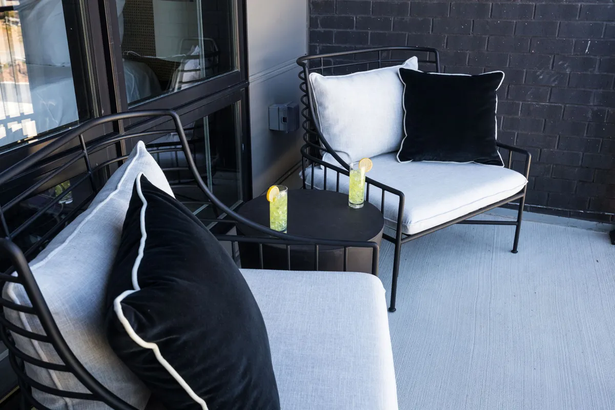 A chic outdoor setting with modern metal chairs and black-and-white cushions surrounding a small table set with cocktails. The ambiance is sophisticated yet relaxed, suggesting sunset gatherings or intimate conversations under the open sky.